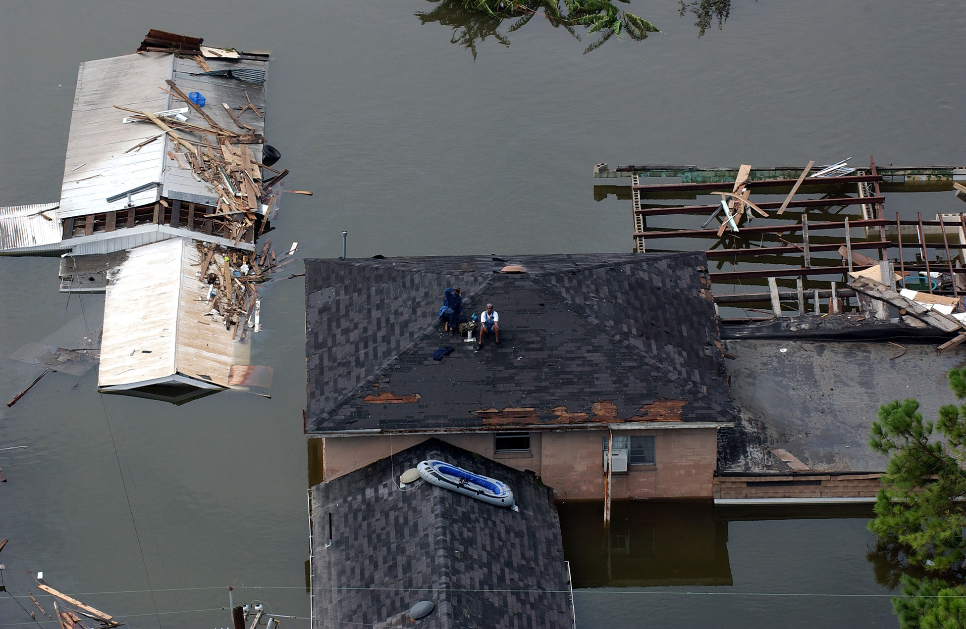 Two people sit on the roof of their house surrounded by floodwater and debris.