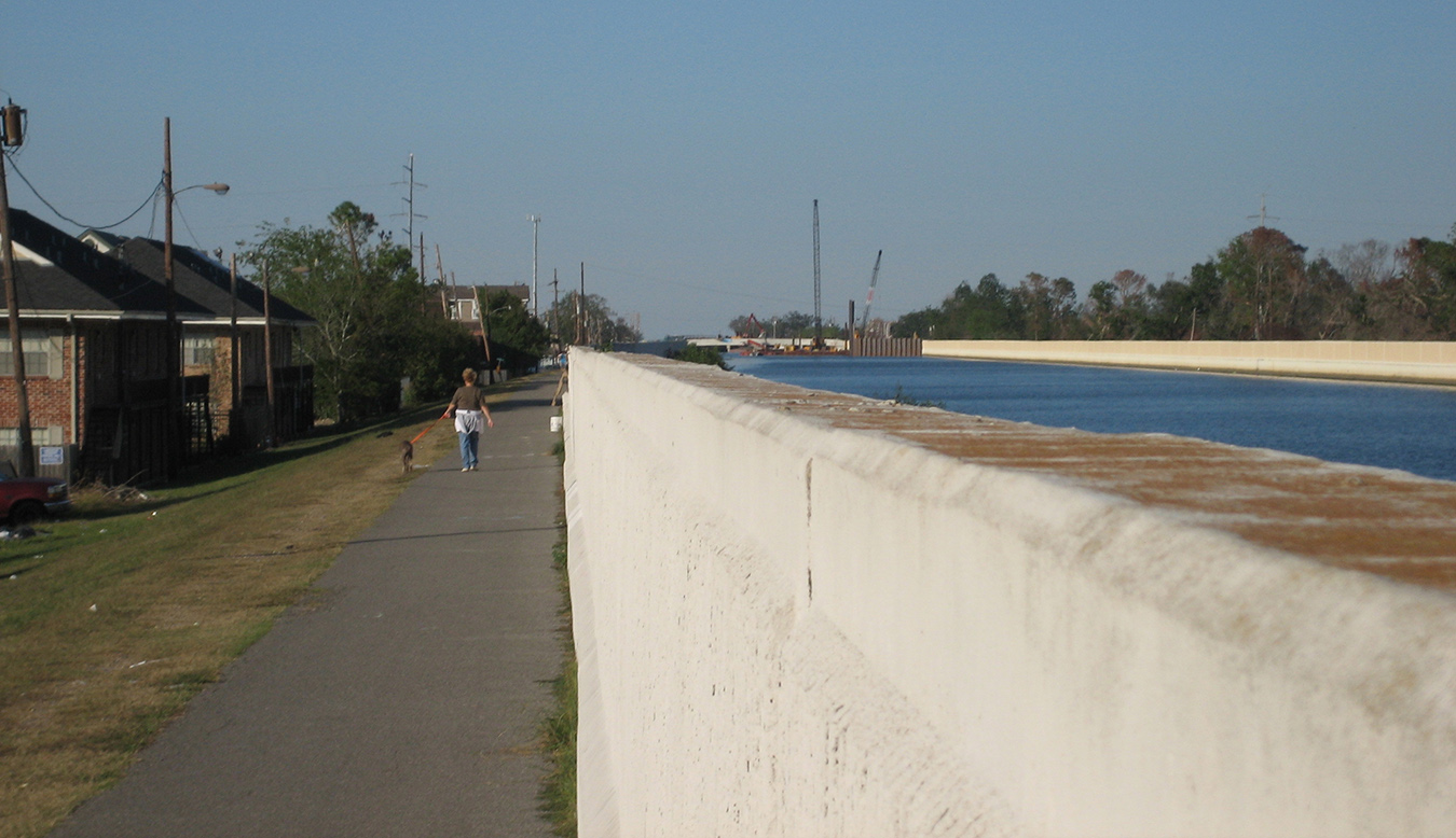 A woman walks her dog next to the high floodwall of a canal