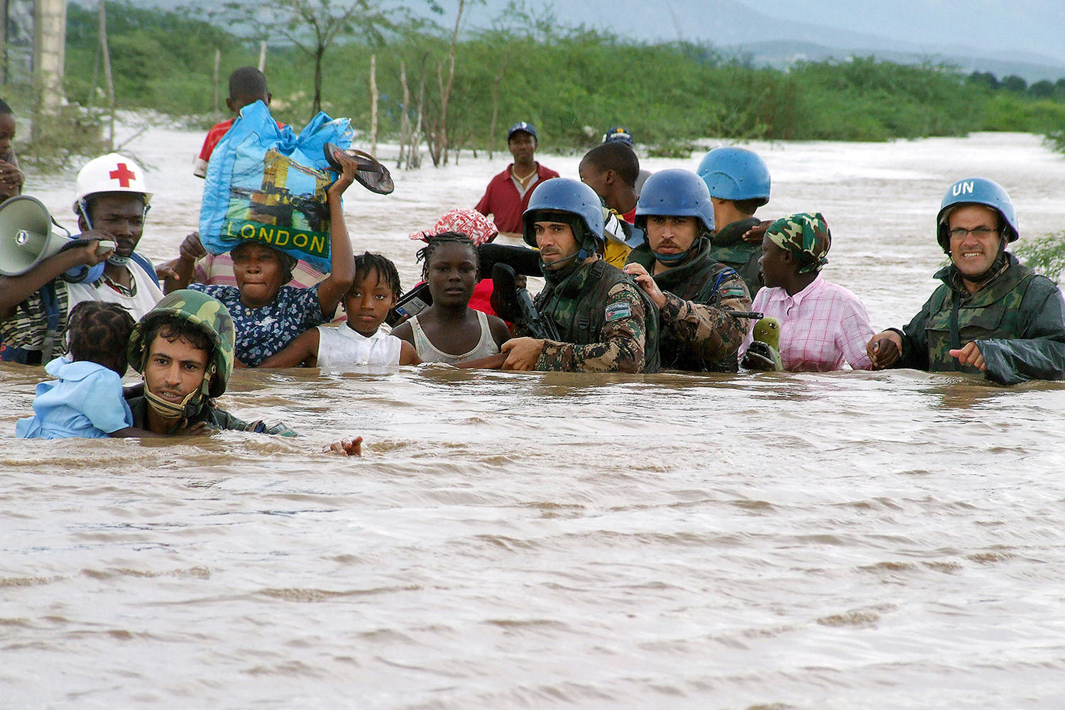Soldiers and children walk through chest-high, brown flood water.